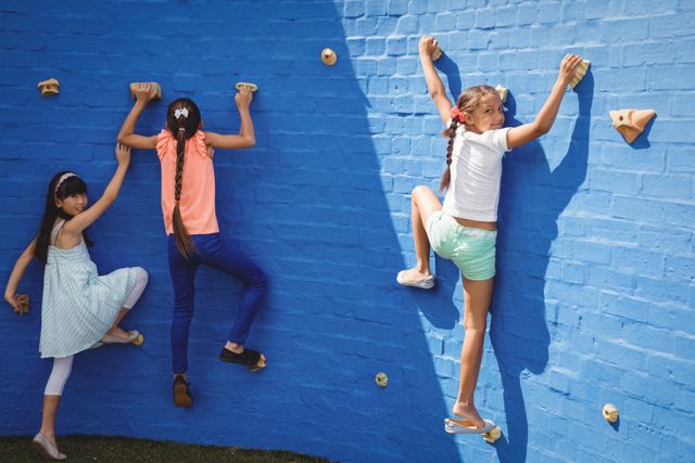 Children climbing a wall at a school playground, engaging in physical activity and teamwork. Ideal for use in educational materials, fitness and health promotions, and advertisements for children's outdoor activities and sports equipment.