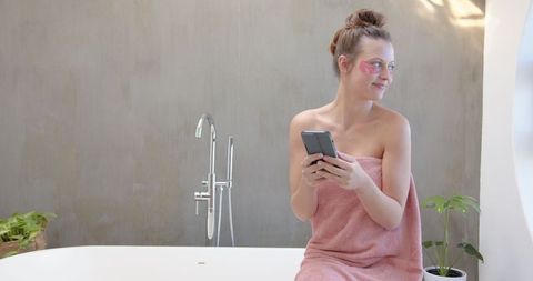 Smiling Woman with Smartphone Relaxing with Skincare in Minimalist Light Bathroom
