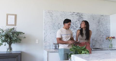 Couple planning home project standing at marble kitchen island with tablet and plants