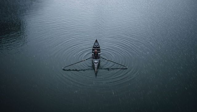 Rowing single scull slicing rain-slick water, solitary sculler with red hat