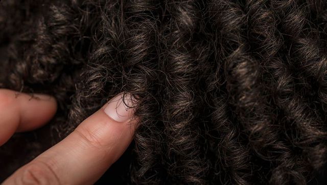 Pressing fingertip into tightly coiled dark curls showing macro texture shine and scalp detail