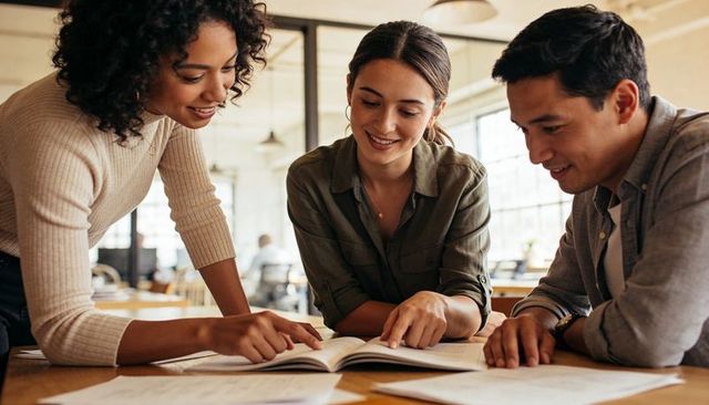 Young professionals collaborating over documents and open book in modern coworking office