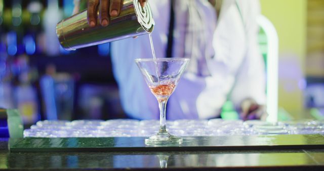 Image of midsection of african american barman poring pink cocktail at the bar. Drinking, inclusivity, going out and alcohol concept.