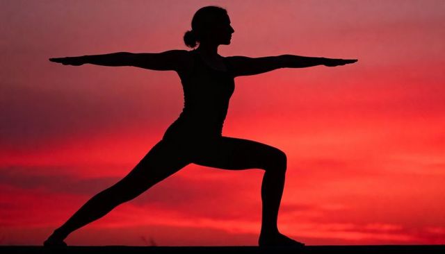 Silhouette woman practicing warrior ii yoga at fiery red sunset horizon for wellness