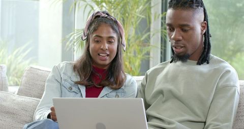 African American man and Indian woman using laptop on sofa discussing online shopping
