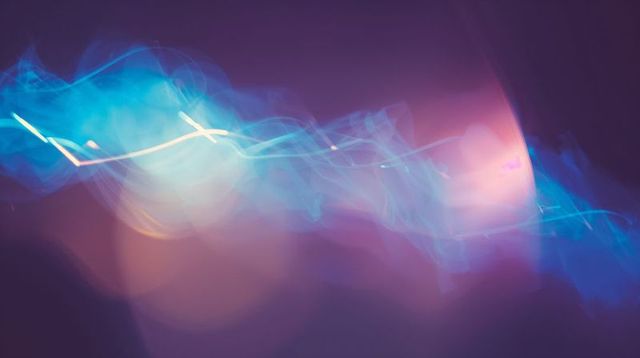 Neon light ribbon flowing across purple gradient background with iridescent bokeh glow