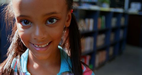 Happy schoolgirl with backpack in library smiling at camera