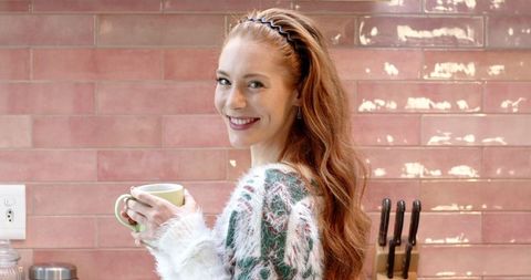 Smiling woman in cozy sweater holding mug in modern kitchen