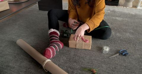 Woman wrapping holiday gift in cozy living room