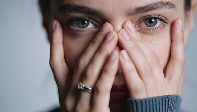 Woman covering face revealing green-gray eyes and solitaire ring, intimate portrait soft light