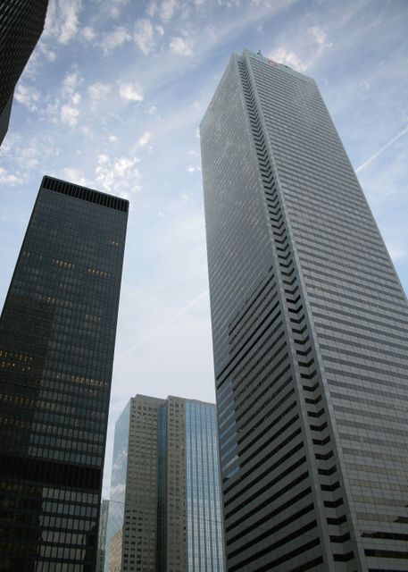 Depicts tall skyscrapers against a partly cloudy sky, perfect for use in presentations about urban development, business districts, corporate offices, or city planning. Suitable for websites, brochures, and articles related to architecture, construction, urbanization, and real estate.