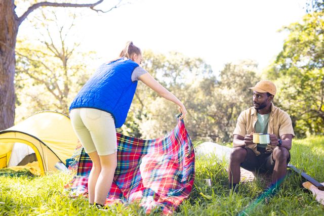 Diverse couple enjoying a sunny day in the park, setting up a picnic with a tent in the background. Perfect for themes related to outdoor activities, camping, leisure, and spending quality time with loved ones. Ideal for use in lifestyle blogs, travel websites, and advertisements promoting outdoor gear and activities.