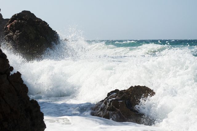 Powerful waves crashing against rocky shoreline with ocean spray. Ideal for use in blogs, travel brochures, and websites that focus on nature, marine environments, and coastal scenery.