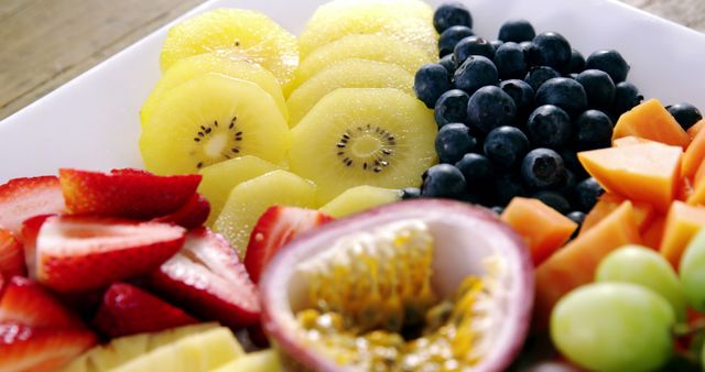 Close-up view of a fresh fruits platter consisting of blueberries, kiwi, passion fruit, strawberries, and grapes. This vibrant and colorful arrangement is perfect for use in menu designs, diet and nutrition blogs, healthy eating campaigns, and cooking magazines to promote wellness and the benefits of fresh fruit.