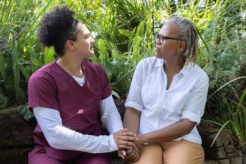 Caregiver holding hands with senior woman on garden bench showing compassion and support