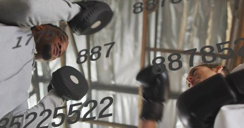 Boxers sparring in gritty industrial gym wearing hoodies and black gloves under rafters