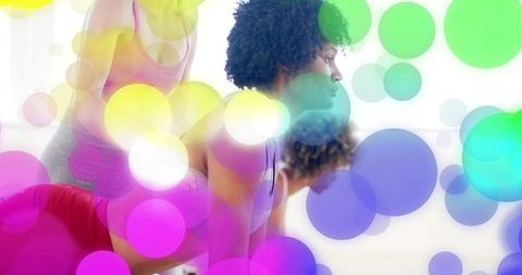 Black woman holding low plank in group fitness studio class with colorful bokeh overlay