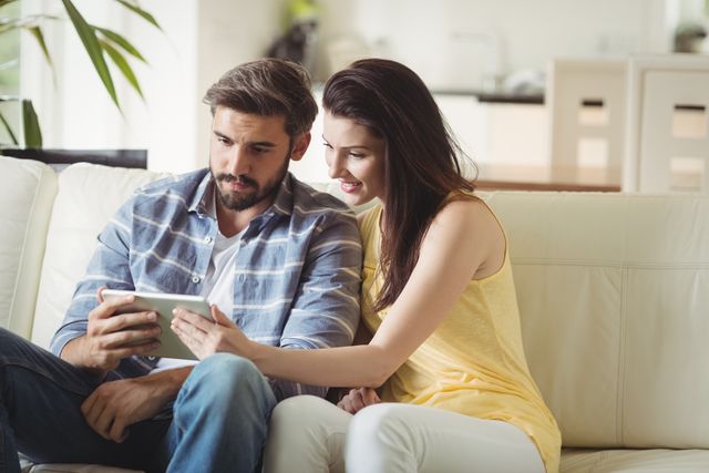 Couple sitting on sofa using digital tablet, ideal for lifestyle blogs, technology advertisements, and home decor magazines. Perfect for illustrating modern living, family bonding, and leisure activities.