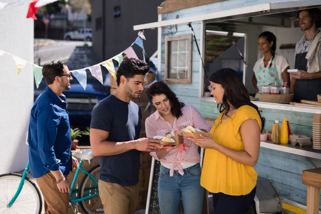 Group of friends enjoying a casual meal at a food truck. Three people are sharing snacks, standing near the food truck's ordering window. Festive bunting is hanging above them, and the scene looks lively and fun. Ideal for depicting outdoor dining, social interactions, and urban lifestyle.
