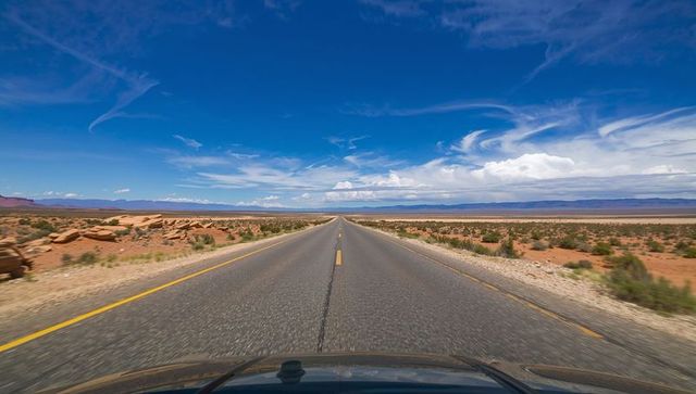 Driving down endless desert highway beneath dramatic blue sky with visible vehicle hood