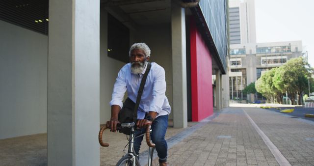Elderly man with a white beard rides a bicycle in a city environment, demonstrating active and healthy living. Ideal for use in ads or articles about sustainable transportation, urban commuting, senior fitness, and independent living.