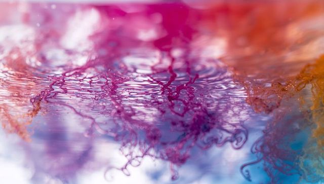 Multicolor ink plumes swirling under rippled water with vibrant pink purple orange blue light