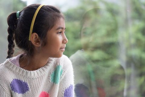 Asian girl gazing through window with reflected portrait and pastel polka-dot sweater