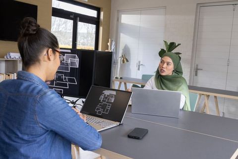 Multicultural women collaborating on architectural plans and blueprints in modern office