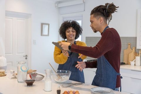 African american couple baking together in sunlit modern kitchen checking tablet