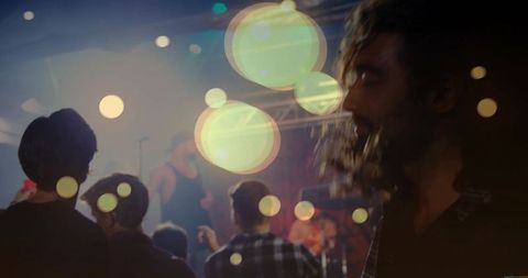 Bearded man enjoying live nightclub concert with bokeh lights