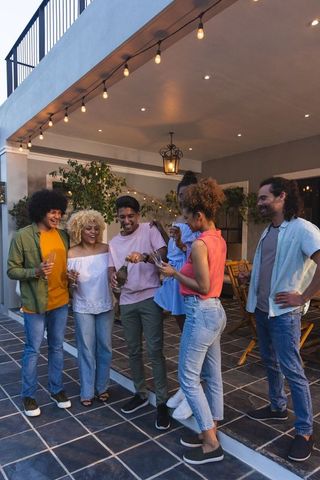 Multiracial friends gathering on tiled patio at dusk under string lights toasting wine