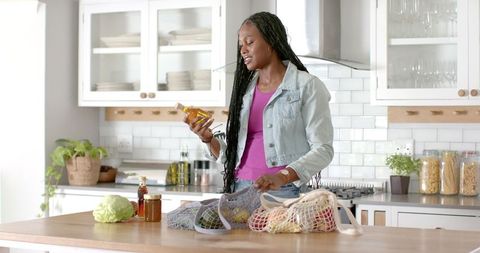 Woman Unpacking Groceries and Holding Bottle of Oil in Modern Kitchen