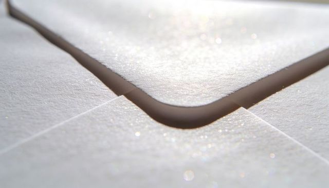 Close-up showing white envelope flap with rounded corner, papery fiber texture and sparkle