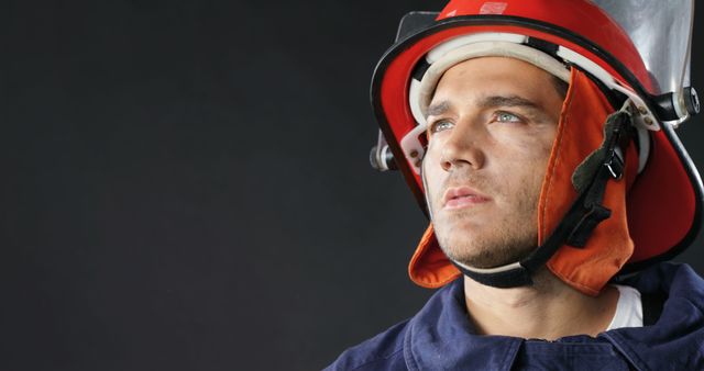 Biracial male firefighter wearing hardhat and protecting suit and looking up, copy space. Fire prevention, professionals, safety and expression concept, unaltered.