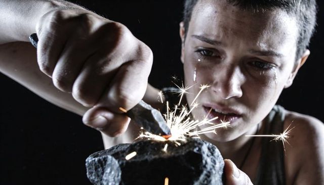 Teen striking metal on stone creating sparks while crying dramatic moody close-up