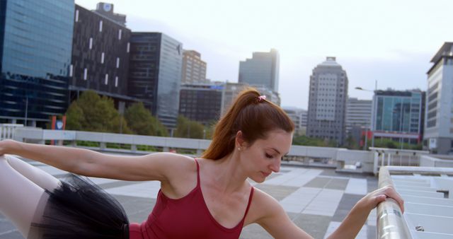 Ballerina stretches outdoors, with copy space. She practices her routine against an urban skyline backdrop.