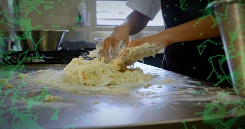 Chef kneading sticky dough on stainless steel counter in commercial kitchen with flour