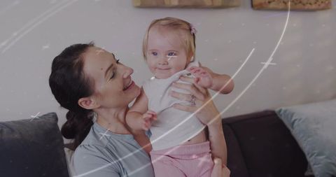 Mother holding smiling baby girl on couch sharing warm family bonding and nurturing moment