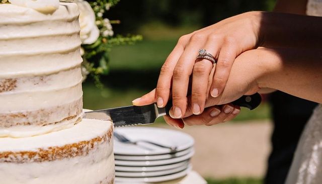 Couple cutting rustic naked wedding cake together showing bridal rings and serrated knife