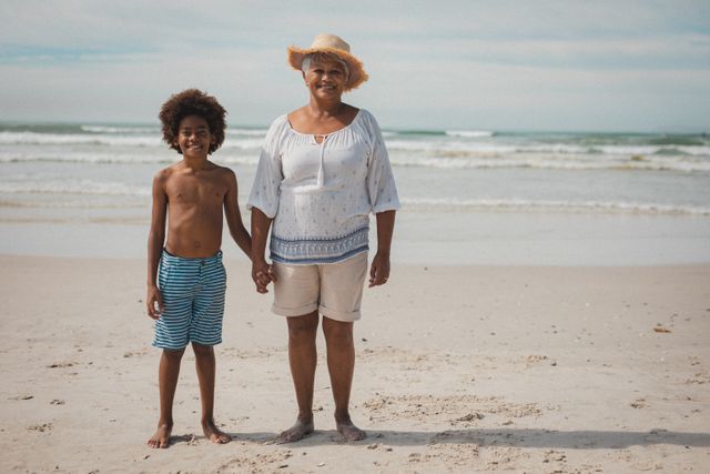 Grandmother and grandson enjoying a sunny day at the beach, smiling and holding hands. Perfect for promoting family vacations, summer holidays, and multigenerational bonding. Ideal for travel brochures, family-oriented advertisements, and lifestyle blogs.