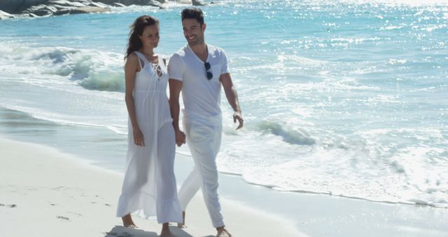 Romantic couple holding hands while strolling on beach wearing white outfits, enjoying summer vacation. Ideal for advertising travel destinations, summer retreats, romantic getaways or lifestyle content documenting couples' moments of happiness and togetherness by the ocean.