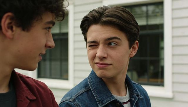Teenage friends exchanging playful wink and smirk outdoors with denim and maroon jackets