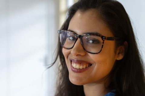 Smiling young woman wearing tortoiseshell glasses posing by window with soft natural light