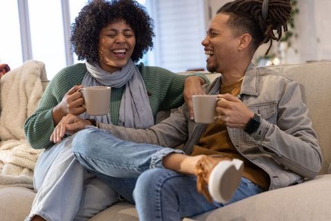 African american couple sharing coffee and laughing on cozy beige sofa in living room