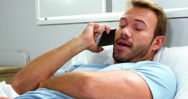 Relaxed man talking on smartphone while lying on bed at home - Download Free Stock Images Pikwizard.com