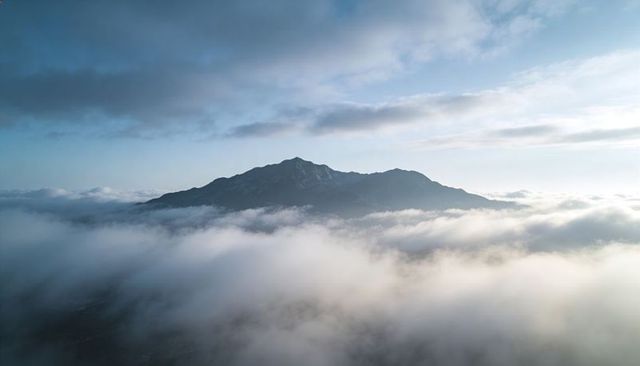 Solitary mountain ridge rising above sea of clouds at dawn aerial misty panorama