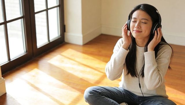 Young woman listening to music on headphones while relaxing on sunlit hardwood floor