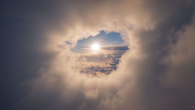Sun shining through circular cloud opening over golden cloudscape, rays streaming outward