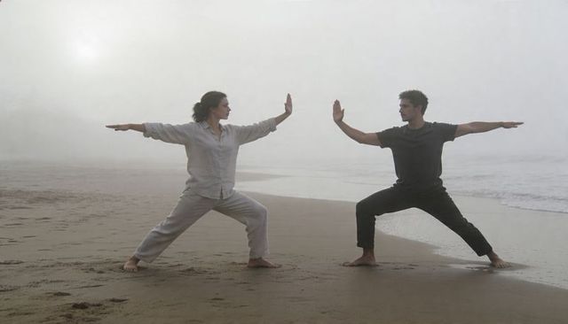 Couple practicing tai chi mirroring on foggy shoreline at sunrise promoting mindful balance