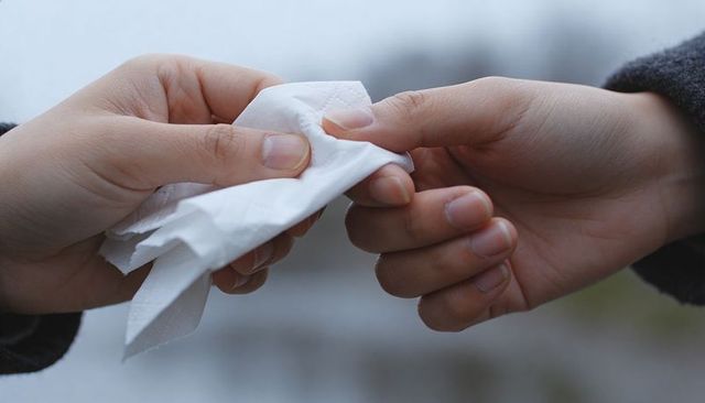 Two hands passing tissue outdoors closeup exchanging napkin handoff conveying compassion